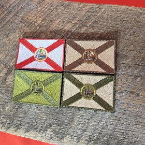 以下が含まれることがあります： フロリダ州の州旗が刺繍されたパッチが4つあります。パッチは、白と赤、茶色とベージュ、緑とベージュ、ベージュと緑の異なる色の組み合わせになっています。