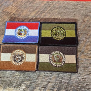 以下が含まれることがあります： コロンビア特別区の旗をデザインした刺繍パッチが4つ。パッチは茶色、黒、ベージュ、青で、中央には金色と白の紋章があります。