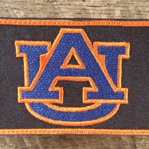 May include: Embroidered patch featuring the Auburn University logo. The patch has a navy blue background with the letter "A" in blue and orange. The border is orange.