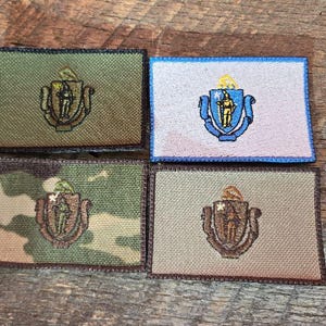May include: Four rectangular embroidered patches featuring the Massachusetts state seal. The patches are in various colors, including green, camouflage, tan, and white with blue trim. Each patch has a brown border.