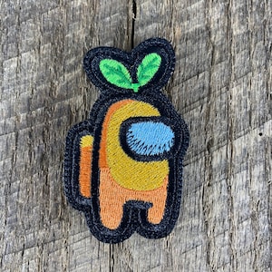 May include: Orange and yellow embroidered patch of a character from the video game Among Us. The character has a black outline and a blue visor. The character has a green sprout on top of its head.