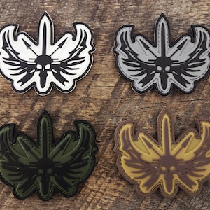 May include: Four tactical morale patches featuring a central skull design with wings and a vertical sword. The patches are rendered in four distinct color combinations: white and black, gray and black, olive green and black, and tan and brown.