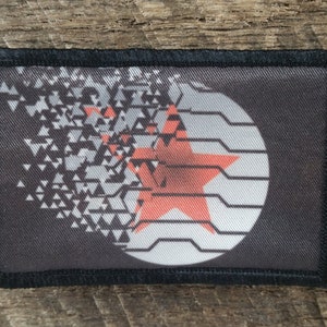 Peut inclure: Un patch noir et blanc avec une étoile rouge au centre. L'étoile est à l'intérieur d'un cercle avec un motif de lignes. Le patch est en tissu et a une bordure noire.