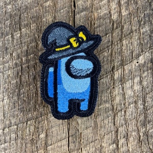 Puede incluir: Un parche bordado azul y negro de un personaje de Among Us que lleva un sombrero de bruja negro con una insignia "FBI" amarilla.