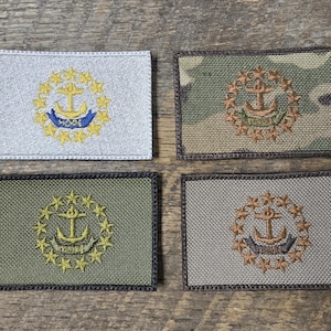 Puede incluir: Cuatro parches rectangulares bordados con diseños de anclas y estrellas. Los parches son de varios colores, incluyendo plateado, camuflaje, verde oliva y gris. El ancla está rodeada por una corona de estrellas.