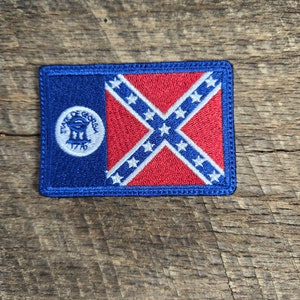 May include: A blue and red embroidered patch with the Confederate flag and the seal of the State of Georgia. The seal is a circle with the words "State of Georgia" and "1776" around the edge. The seal depicts a three-masted ship with a flag flying from the mast.