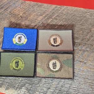 Peut inclure: Quatre patchs brodés représentant le sceau de l'État du Dakota du Nord. Les patchs sont de couleurs et de matières différentes, notamment bleu, beige, vert et camouflage.