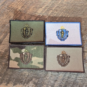 Può includere: Quattro toppe ricamate con il sigillo dello stato del Massachusetts. Le toppe sono di diversi colori e motivi, tra cui verde, blu, mimetico e beige.