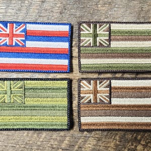Puede incluir: Cuatro parches rectangulares bordados con el diseño de la bandera hawaiana. Un parche tiene las tradicionales rayas rojas, blancas y azules con una Union Jack en la esquina. Los otros tres parches tienen un diseño similar pero con diferentes combinaciones de colores.