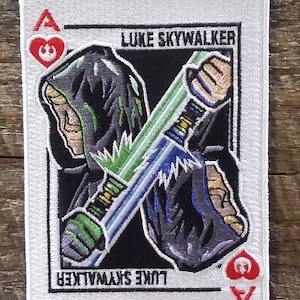 May include: White patch featuring Luke Skywalker from Star Wars, depicted as the Ace of Hearts playing card. The design includes a hooded figure, crossed lightsabers, and the text "LUKE SKYWALKER". The Ace of Hearts symbol is in the corners.