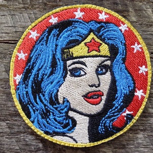 May include: Embroidered patch featuring Wonder Woman with a red, white, and yellow star-shaped headband. The patch is circular with a red background and white stars around the edge.