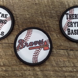 May include: Three round baseball-themed patches. One patch features the text "You're Killing Me Smalls". Another patch features the text "There's No Crying in Baseball!" The third patch features the Atlanta Braves logo with a tomahawk.