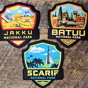 May include: Three shield-shaped patches featuring Star Wars locations. The top left patch shows Jakku National Park with a desert landscape and spacecraft. The top right patch shows Batuu National Park with buildings. The bottom patch shows Scarif National Park with palm trees and a tower.