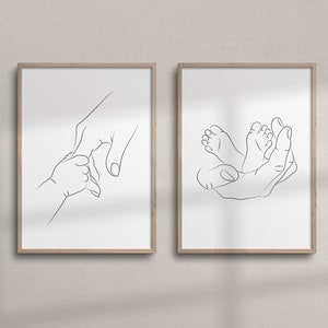 Puede incluir: Dos impresiones art&iacute;sticas enmarcadas con dibujos lineales minimalistas. Una representa la mano de un padre sosteniendo la mano de un beb&eacute;, la otra la mano de un padre acunando los pies de un beb&eacute;. La obra de arte es en blanco y negro.