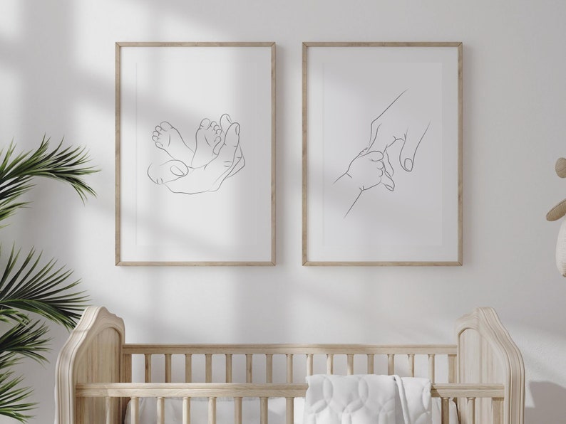 Puede incluir: Dos impresiones art&iacute;sticas enmarcadas con dibujos lineales. Una representa una mano acunando pies de beb&eacute;, la otra una mano sosteniendo la mano de un beb&eacute;. Los marcos son de madera clara y el arte se exhibe en una pared blanca. El tema es beb&eacute; y familia.