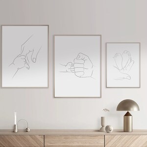 Puede incluir: Tres impresiones minimalistas de arte de l&iacute;nea que representan a un padre y un hijo d&aacute;ndose la mano, un padre y un hijo chocando los pu&ntilde;os y un padre y un hijo toc&aacute;ndose los pies. Las impresiones est&aacute;n enmarcadas en un marco de madera clara y est&aacute;n colgadas en una pared blanca.