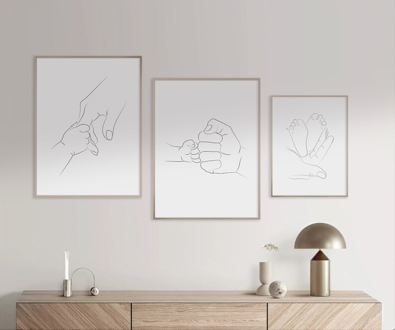 Puede incluir: Tres impresiones minimalistas de arte de l&iacute;nea que representan a un padre y un hijo d&aacute;ndose la mano, un padre y un hijo chocando los pu&ntilde;os y un padre y un hijo toc&aacute;ndose los pies. Las impresiones est&aacute;n enmarcadas en un marco de madera clara y est&aacute;n colgadas en una pared blanca.