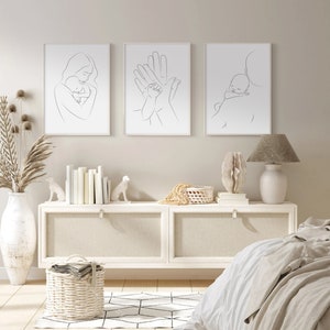 Puede incluir: Tres impresiones minimalistas de arte lineal en marcos blancos que representan a una madre sosteniendo un beb&eacute;, dos manos sosteniendo la mano de un beb&eacute; y un padre llevando a un beb&eacute; dormido sobre su hombro. Las impresiones se muestran en una pared blanca sobre una c&oacute;moda blanca con una l&aacute;mpara blanca en el lado derecho.