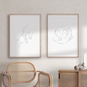 Puede incluir: Dos grabados enmarcados de arte lineal. Uno representa una mano sosteniendo la mano de un beb&eacute;, el otro muestra los pies del beb&eacute; en una mano. Los grabados est&aacute;n en marcos de madera clara, creando una est&eacute;tica minimalista y conmovedora.