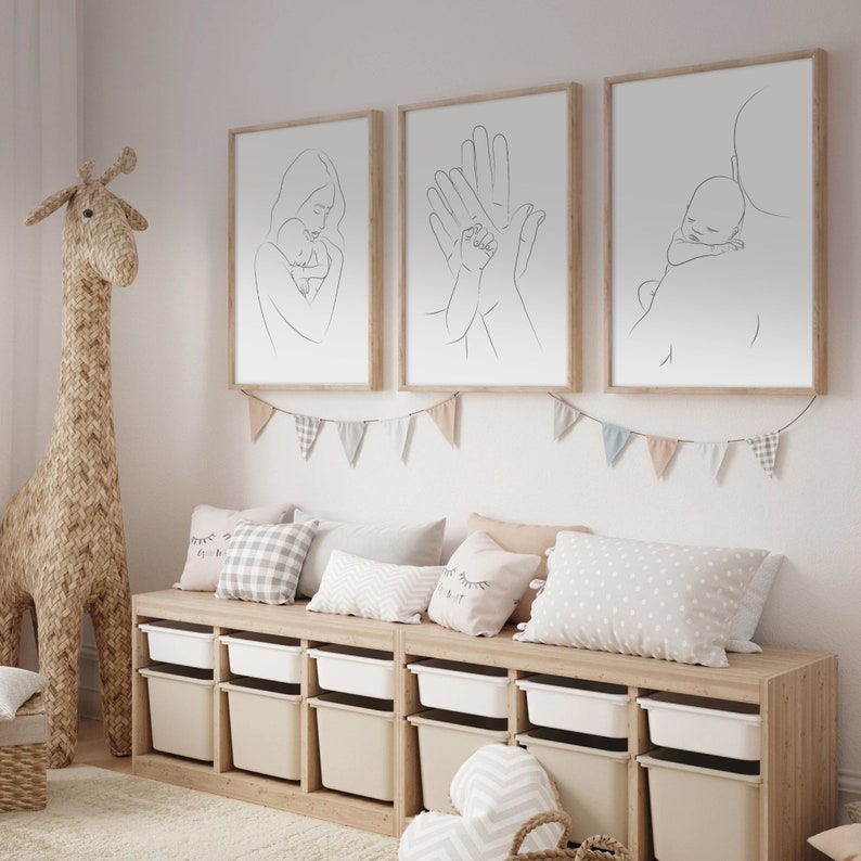 Puede incluir: Tres impresiones minimalistas de arte lineal en marcos de madera colgadas en una pared blanca. Las impresiones representan a una madre sosteniendo un beb&eacute;, dos manos sosteni&eacute;ndose mutuamente y un padre sosteniendo un beb&eacute;. Las impresiones est&aacute;n sobre un banco de madera con contenedores de almacenamiento y almohadas.
