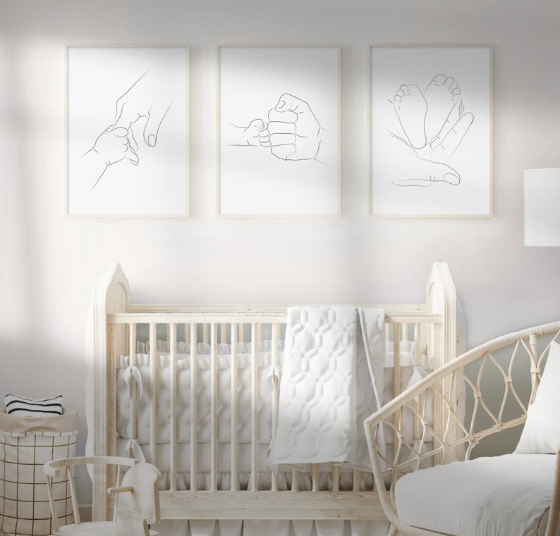 Puede incluir: Tres impresiones minimalistas de arte lineal que representan a un padre sosteniendo la mano de un beb&eacute;, un padre y un beb&eacute; chocando los pu&ntilde;os y un padre sosteniendo los pies de un beb&eacute;. Las impresiones est&aacute;n enmarcadas y colgadas en una pared blanca sobre una cuna blanca.