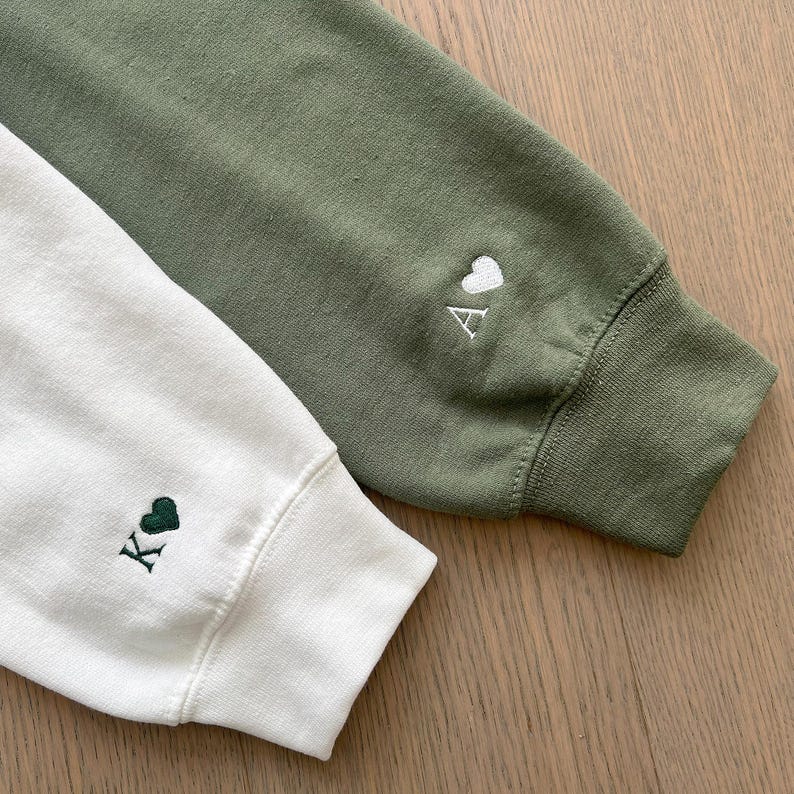 May include: Two sweatshirts with embroidered hearts and letters. One is white with a green heart and the letter K. The other is green with a white heart and the letter A.