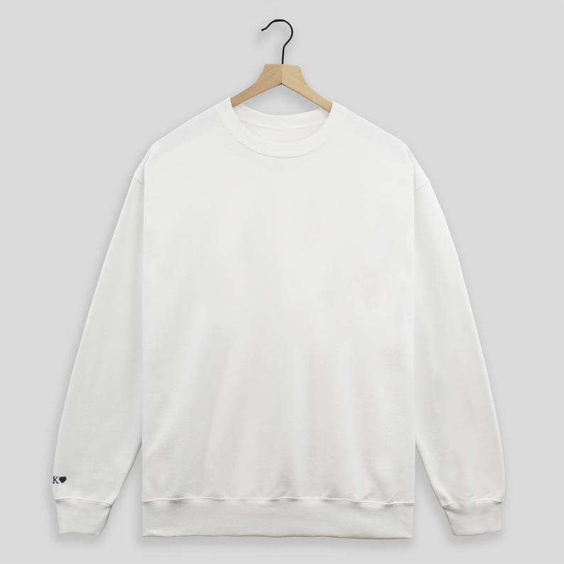 May include: A white crew neck sweatshirt with a small black heart on the left sleeve.