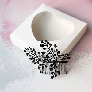 May include: Black hair comb with a fern design. The comb is in a white heart-shaped box.
