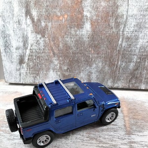 May include: Blue toy truck with a black bed and a silver roof rack. The truck has a spare tire on the back.
