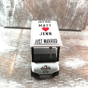 May include: A white golf cart ornament with the words "DATE HERE", "MATT", a red heart, "JENN", and "JUST MARRIED" printed on the roof. The front of the cart has the word "4EVER" on the license plate.