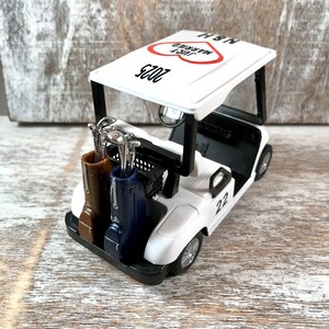 May include: White golf cart with a red heart and the text "Just Married" and "2023" on the roof. The cart has two golf bags and a number "22" on the side.