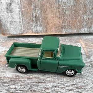 May include: A green vintage pickup truck toy with a detailed design. The truck features a classic cab, bed, and wheels with chrome accents. The toy truck is a miniature replica of a classic vehicle.