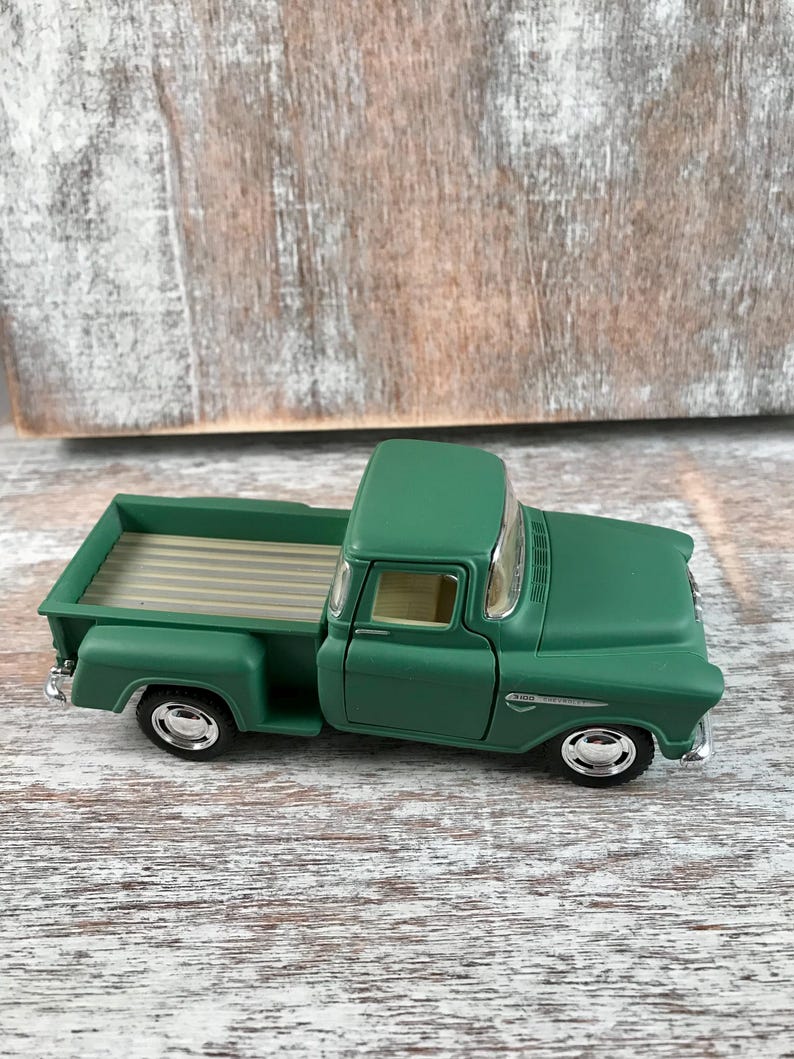 May include: A green vintage pickup truck toy with a detailed design. The truck features a classic cab, bed, and wheels with chrome accents. The toy truck is a miniature replica of a classic vehicle.
