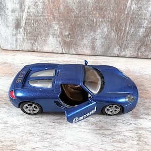 Puede incluir: Un coche de juguete azul con la puerta abierta, que revela un interior marr&oacute;n. El coche tiene ruedas plateadas y la palabra "Samuel" est&aacute; escrita en la puerta. El a&ntilde;o "2018" est&aacute; impreso en la parte trasera del coche.