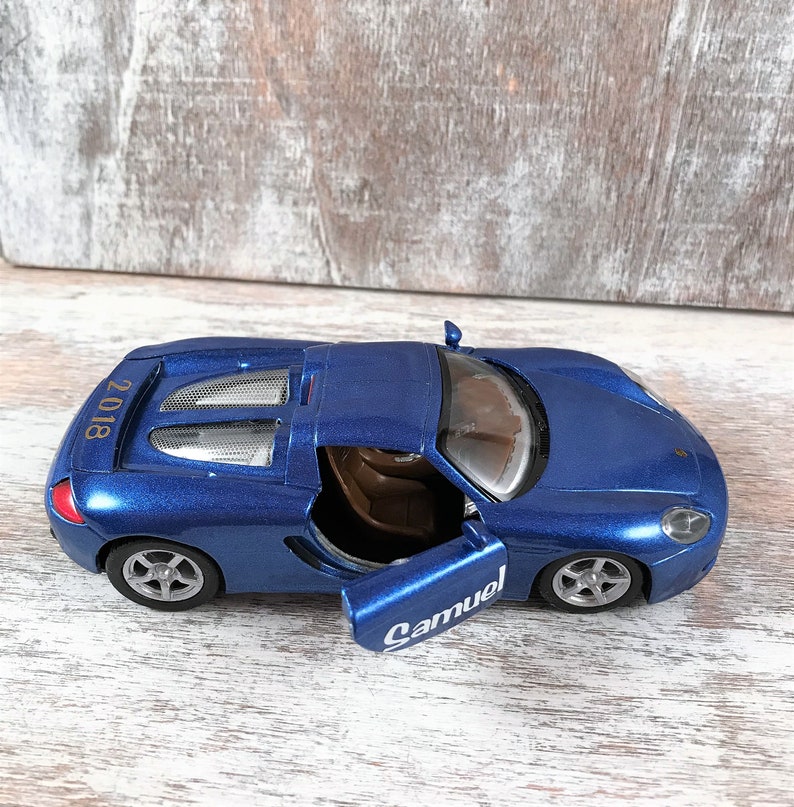 Puede incluir: Un coche de juguete azul con la puerta abierta, que revela un interior marr&oacute;n. El coche tiene ruedas plateadas y la palabra "Samuel" est&aacute; escrita en la puerta. El a&ntilde;o "2018" est&aacute; impreso en la parte trasera del coche.