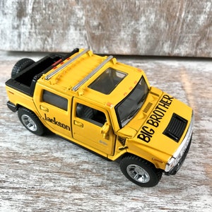 May include: Yellow toy Hummer with a black roof rack and a black grill. The toy truck has a black and white sticker that says "Big Brother" and a sticker that says "Jackson".
