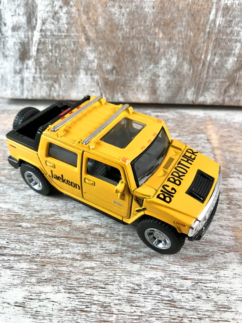 May include: Yellow toy Hummer with a black roof rack and a black grill. The toy truck has a black and white sticker that says "Big Brother" and a sticker that says "Jackson".