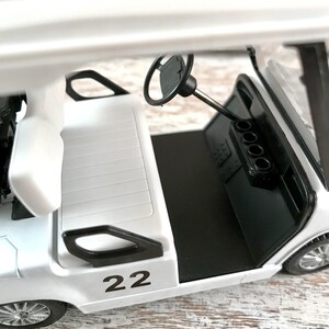 May include: A white golf cart toy with black accents, including the steering wheel and dashboard. The number "22" is printed in black on the side. The cart has a black floor and silver wheels.