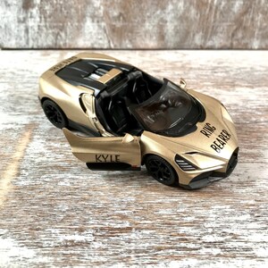 May include: A gold-colored toy convertible car with black wheels and interior. The car's door is open, revealing the name "KYLE" printed on the side. The words "RING BEARER" are printed on the front.