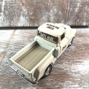 May include: A cream-colored toy pickup truck with the words "DATE HERE" on the windshield and "RING BEARER" on the roof. The truck bed is beige with wooden slats. The truck has chrome details.
