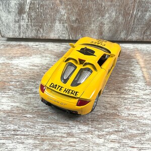 Puede incluir: Un coche de juguete amarillo con el texto "DATE HERE" y "Carrera GT" impreso en la parte trasera. El coche tiene detalles en negro y un interior negro. Las palabras "CLASS OF 2006" est&aacute;n impresas en la parte superior del coche.