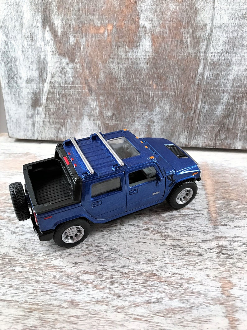 May include: Blue toy truck with a black bed and a silver roof rack. The truck has a spare tire on the back.