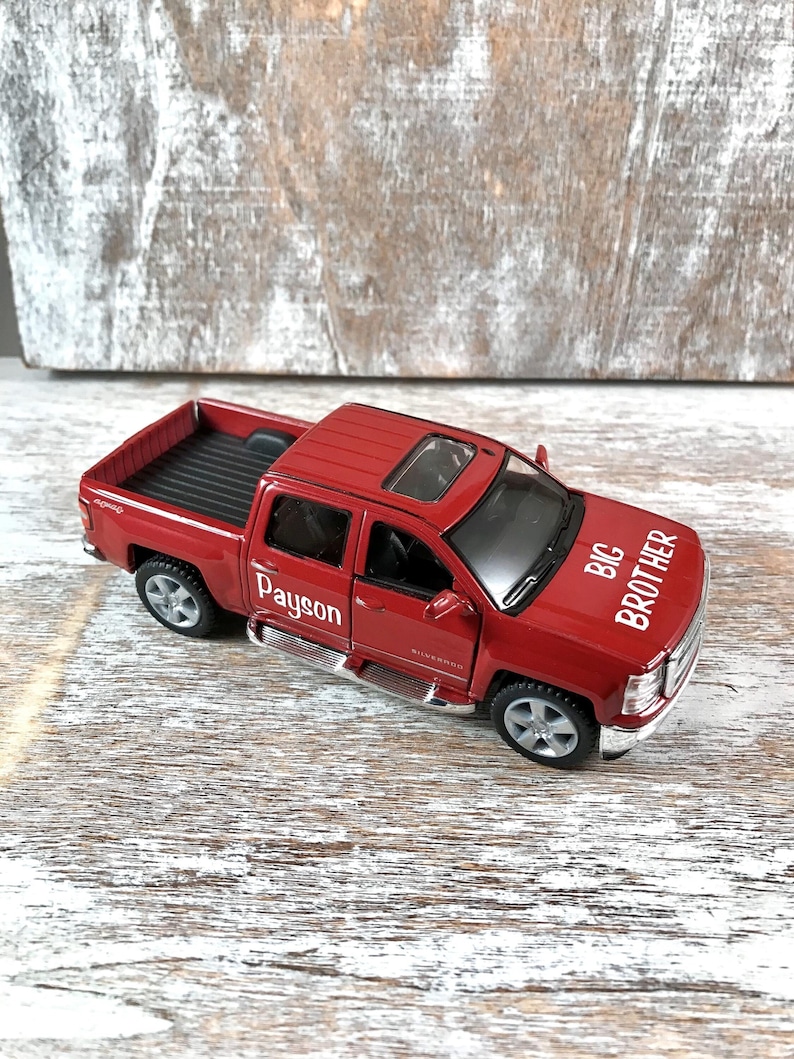 May include: Red toy pickup truck with a black bed and a sunroof. The truck has "Payson" and "Big Brother" written on the sides.