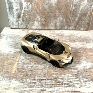 May include: A gold-colored toy convertible car with black accents. The car has the words "RING BEARER" and "KYLE" printed on it. The car is sitting on a white and gray wooden surface.
