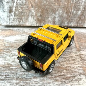May include: Yellow toy truck with a black bed and a silver roof rack. The truck has a black spare tire on the back and the word "Jackson" written on the side.