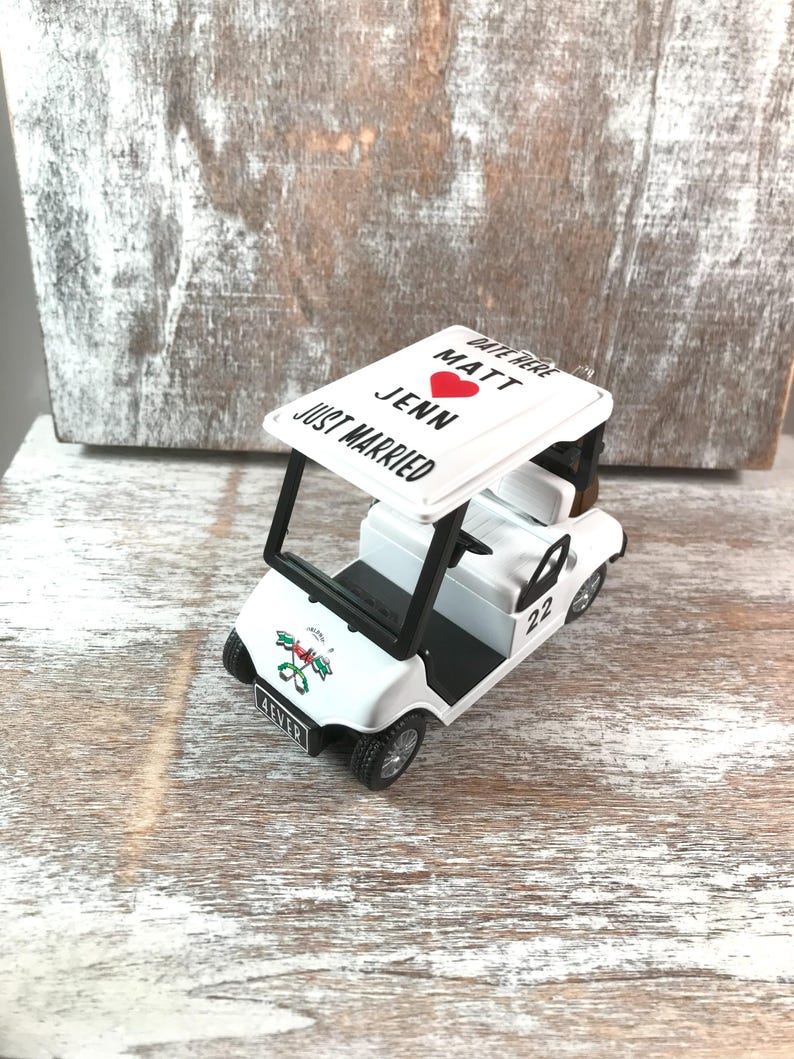 May include: A white toy golf cart with black accents, featuring the text "JUST MARRIED" and names "Matt" and "Jenn" with a red heart. The cart has the number "22" on the side and the word "4EVER" on the front.
