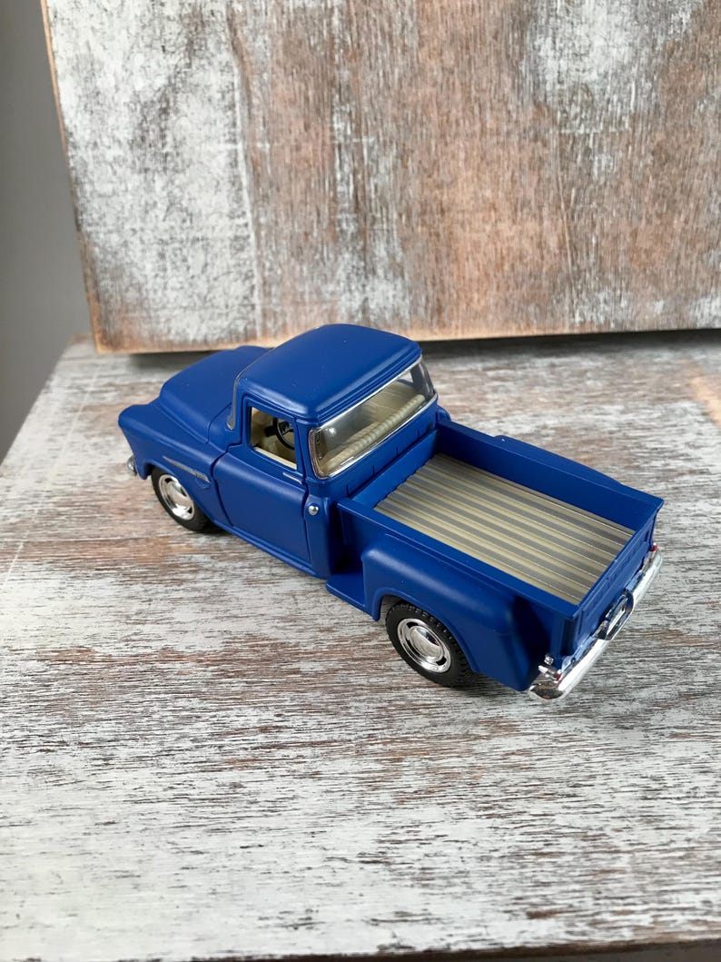 May include: A die-cast model of a classic blue pickup truck. The truck features a detailed interior, chrome accents, and a tan bed. The vehicle is a vintage style, with a glossy finish and realistic design.