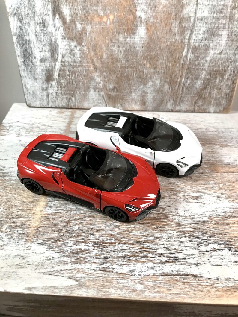 May include: Two toy sports cars, one red and one white, are displayed on a distressed wooden surface. The red car has black accents and a black interior. The white car has black accents and a black interior. Both cars have a sleek, modern design.