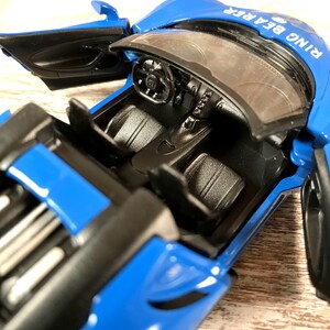 May include: A blue toy car with the doors open, revealing a black interior. The car has the words "RING BEARER" printed on the top. The steering wheel and dashboard are visible.