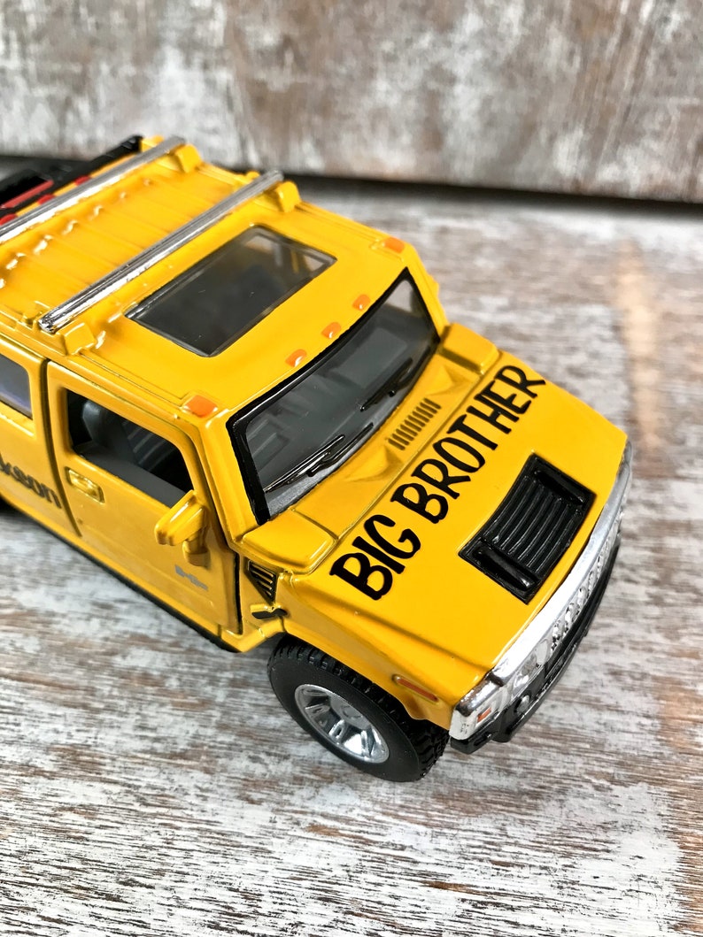 May include: Yellow toy Hummer with a black "BIG BROTHER" decal on the hood. The toy has a black grill, black wheels, and a sunroof.